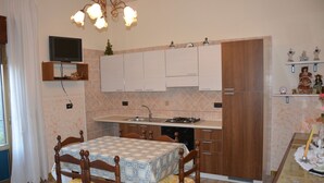 Una cucina con mobili in legno, uno schienale piastrellato, un tavolo da pranzo con sedie, un televisore montato a parete e una piccola mensola con statuine.
