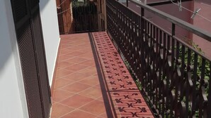 Un balcone stretto con pavimento in tegole rosse e ringhiera in metallo decorativo.