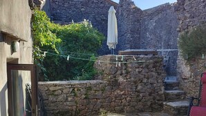 A stone courtyard with a rustic stone wall, a wooden bench, and a table with a white tablecloth. - Casal, very beautiful stone house in the wild steppe of the Causse (Campestre-Et-Luc)