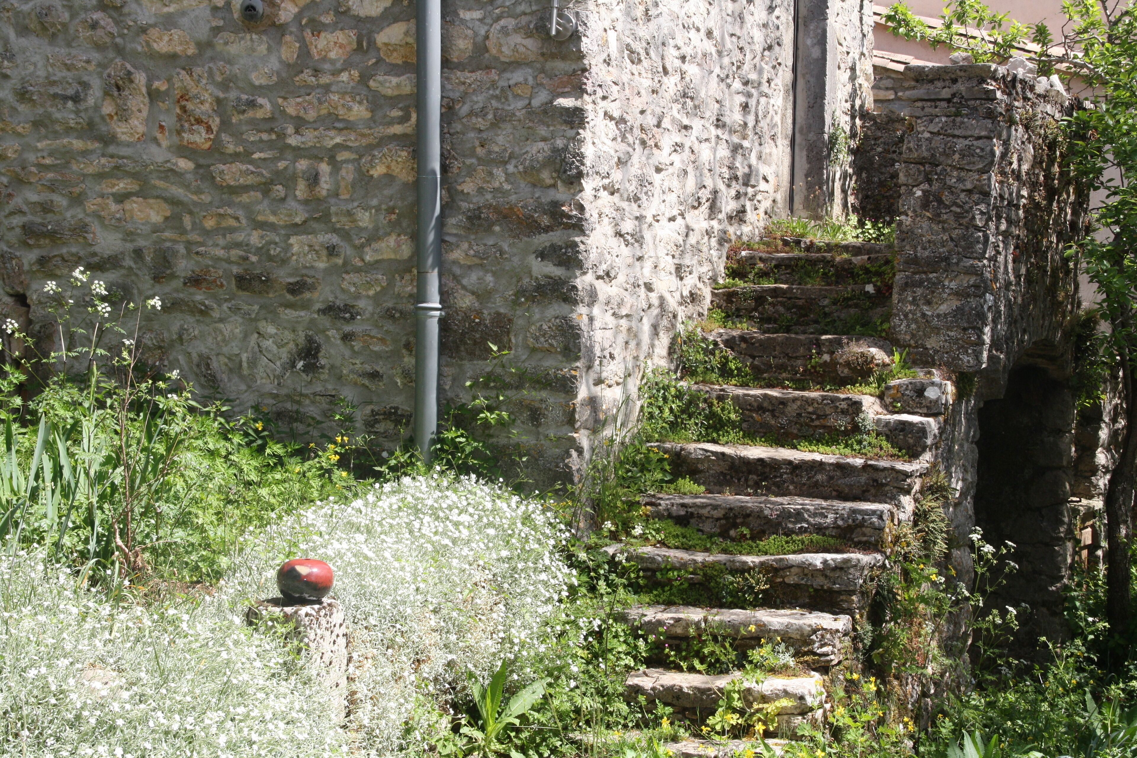 A stone staircase leading up to a building with a stone wall and a pipe running along it.