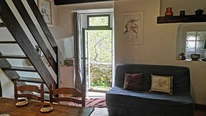 A cozy living room with a wooden staircase, a sofa, and a dining table with plates. - Casal, very beautiful stone house in the wild steppe of the Causse (Campestre-Et-Luc)
