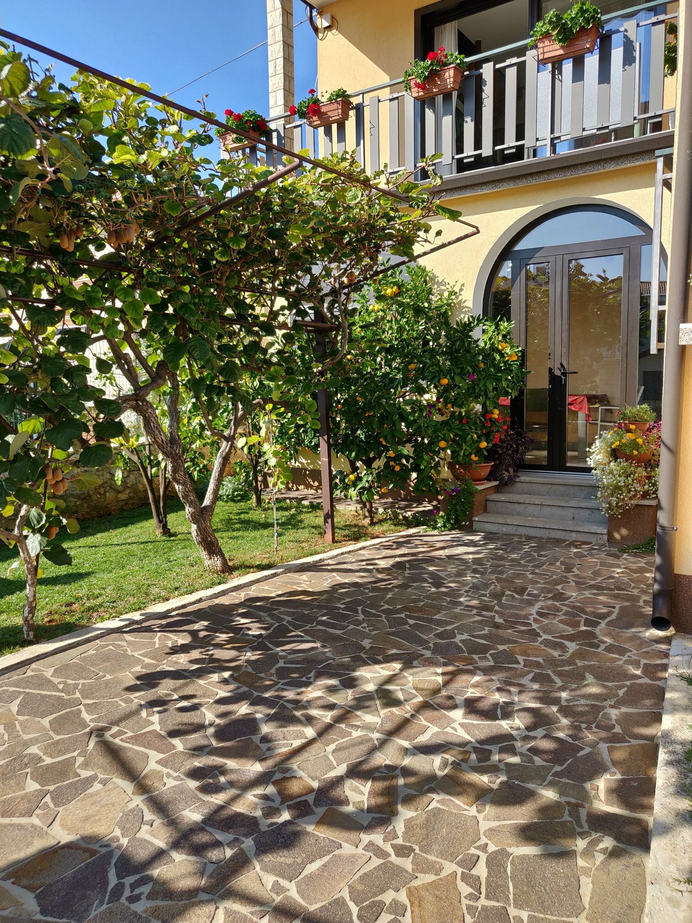 A stone-paved pathway leading to a building with a balcony adorned with potted plants.