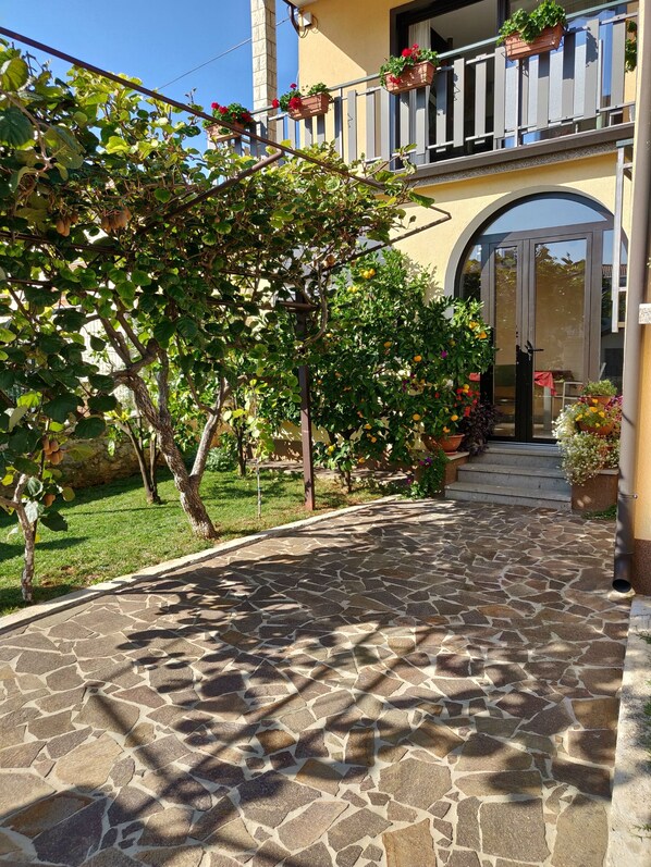 Un sentier pavé de pierres mène à un bâtiment doté d’un balcon orné de plantes en pot.