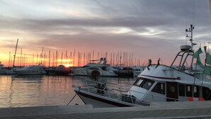 Un port de plaisance où sont amarrés de nombreux bateaux, un coucher de soleil en arrière-plan et un ciel nuageux.
