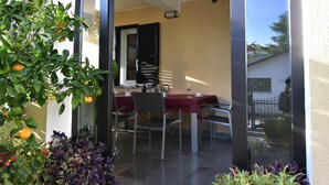 Une porte vitrée donne sur un coin repas, où se trouvent une table et des chaises, le tout étant agrémenté de plantes et de fleurs en pot.