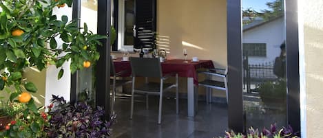 A glass door leading to a dining area with a table and chairs, surrounded by potted plants and flowers.