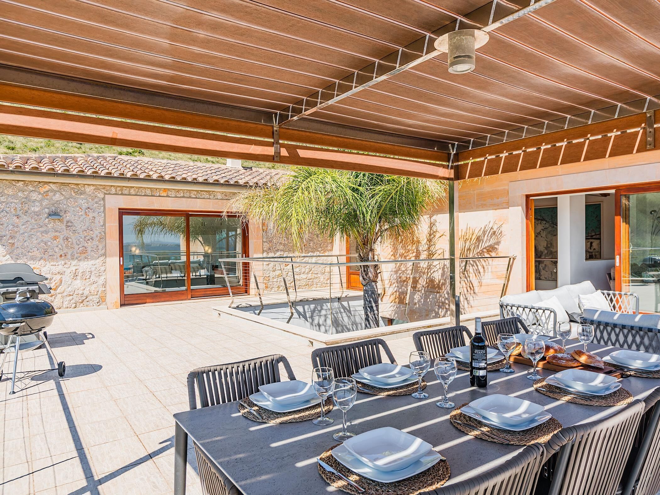An outdoor dining area with a table set for six, surrounded by chairs, and a grill.