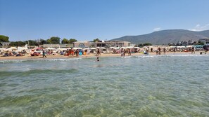 A beach with clear water, umbrellas, and people.