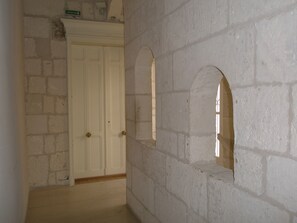 Un couloir avec une porte blanche, un mur de briques et un mur blanc orné de fenêtres en arc de cercle.