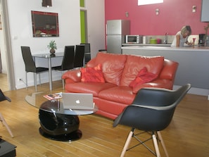 Un salon moderne avec un canapé en cuir rouge, une table basse en verre sur laquelle se trouve un ordinateur portable, et un fauteuil noir.