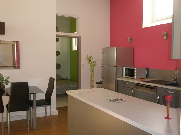A modern kitchen with a white countertop, stainless steel appliances, and a dining area with a table and chairs. - THREE-ROOM APARTMENT 64M2 HYPER CENTER (La Rochelle)