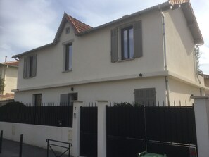 Ein zweigeschossiges Gebäude mit weißer Fassade, einem Ziegeldach und einem schwarzen Metallzaun.