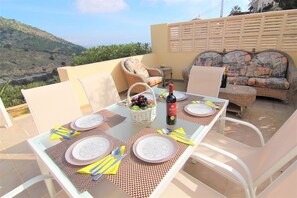 An outdoor dining area with a table set for four, surrounded by wicker chairs and a sofa.