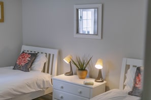 A bedroom with two beds, a bedside table with a lamp, a potted plant, and a window. - Corffe Cottages, Space for all the family, heated indoor pool (Barnstaple)