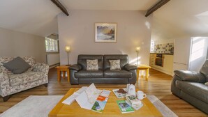 A living room with a sofa, a coffee table with magazines, and a painting on the wall. - Corffe Cottages, Space for all the family, heated indoor pool (Barnstaple)