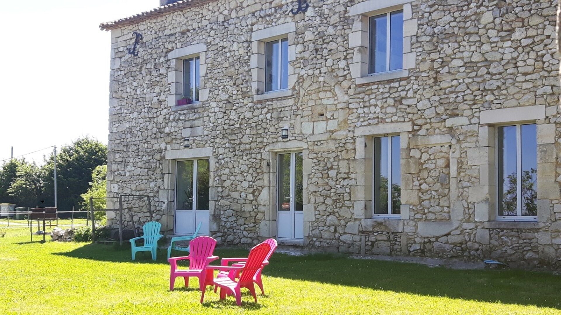 A stone building with multiple windows and a door, a grassy lawn, and outdoor chairs.