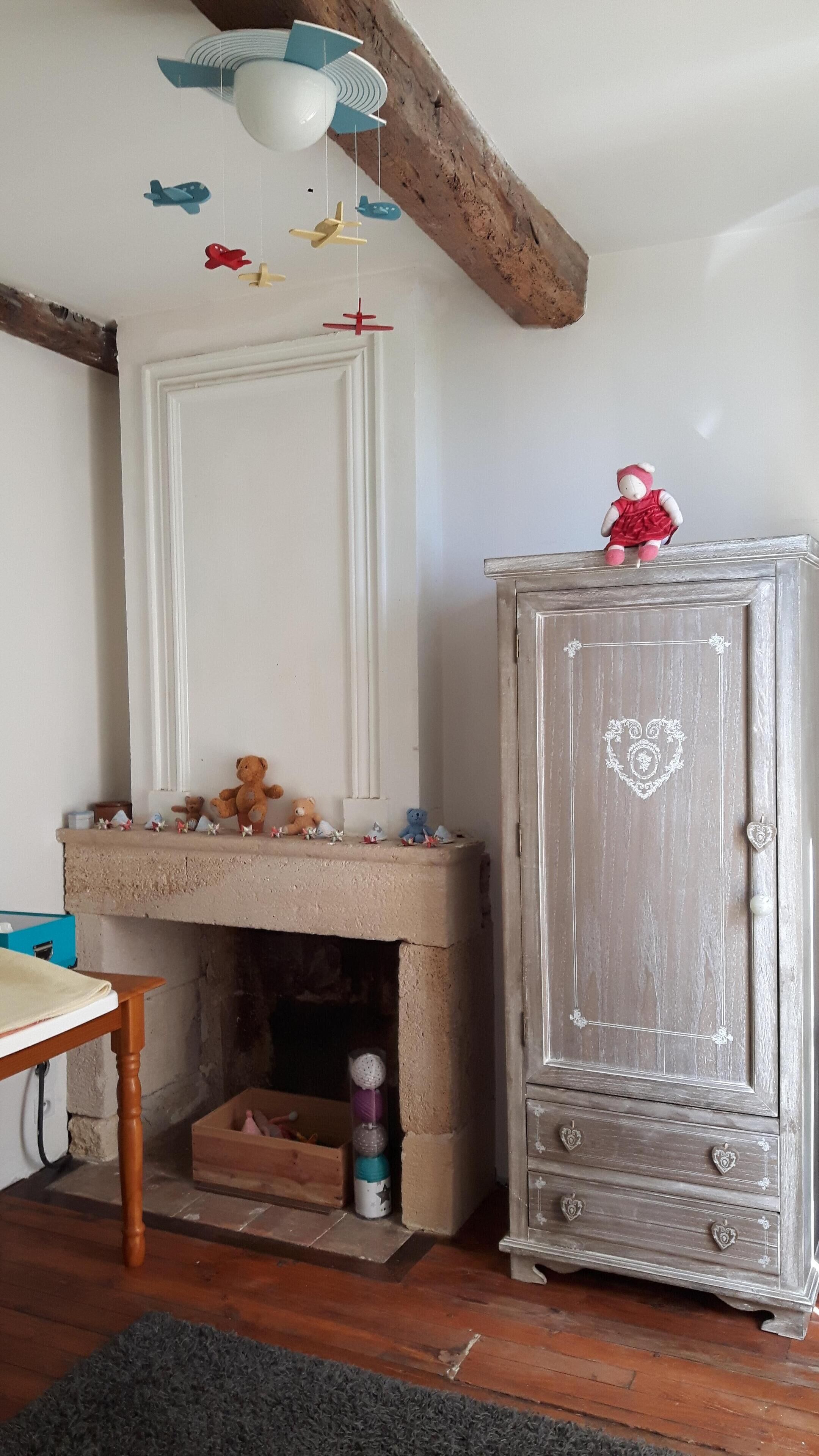 A room with a fireplace, a wooden table, a cabinet with a heart design, and a ceiling fan with hanging airplane decorations.