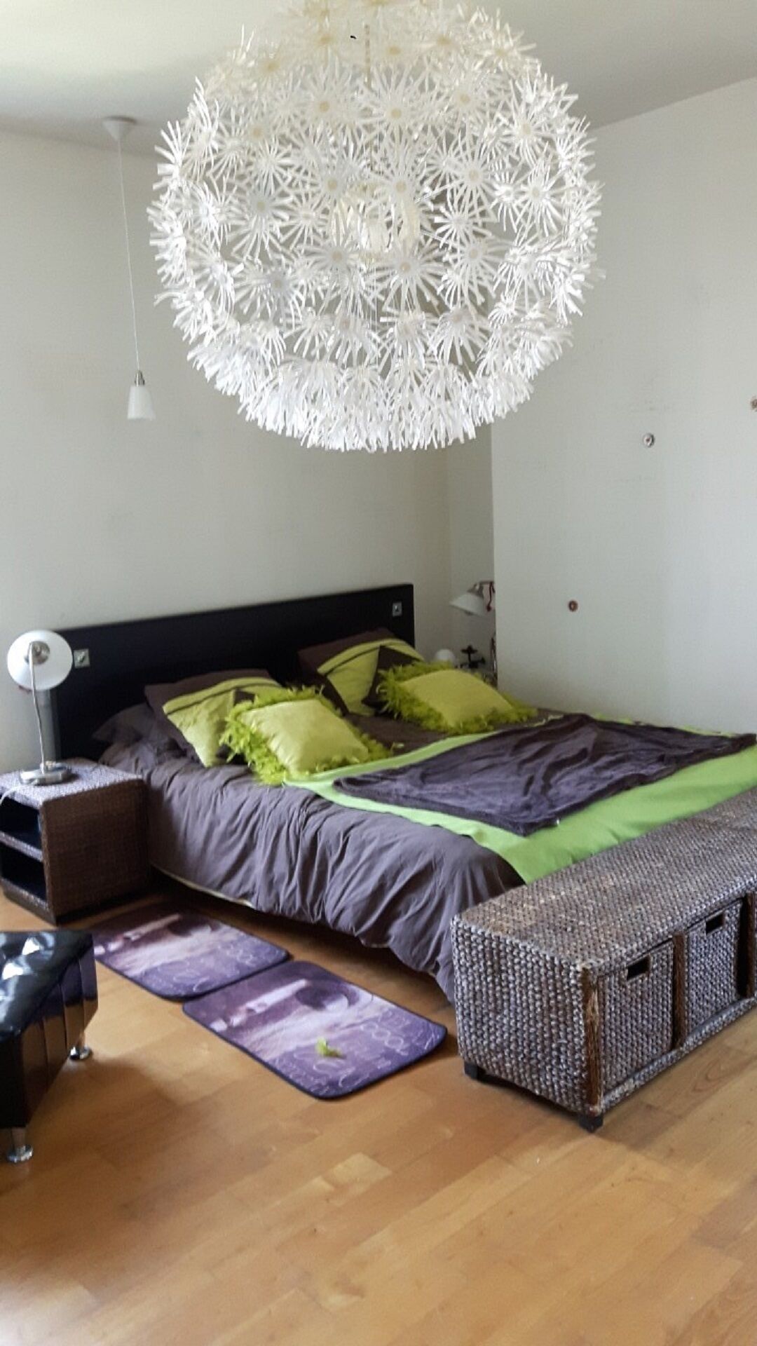 Ein Schlafzimmer mit einem Bett, einem Nachttisch, einer Lampe, einer Pendelleuchte, einem kleinen Teppich und einer gewobenen Bank.