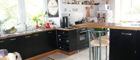A kitchen with black cabinets, a wooden countertop, a sink, a stove, and a refrigerator. There are two bar stools and a window with a view of trees.