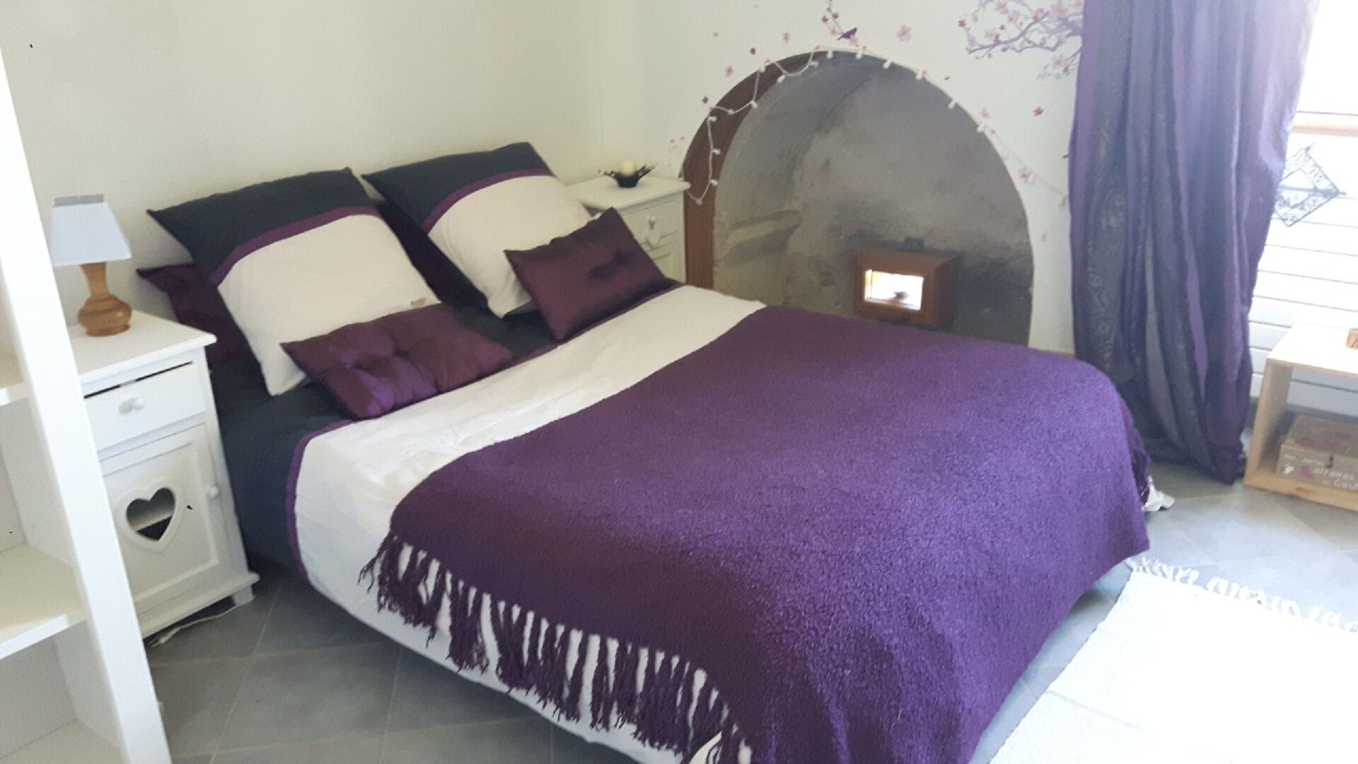 Un dormitorio con una cama, una mesita de noche, un aparador y una chimenea de piedra.
