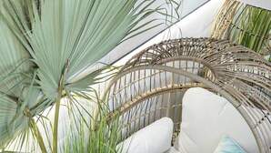 A wicker sofa with cushions, a small round table with a bowl of lemons, and a potted plant.
