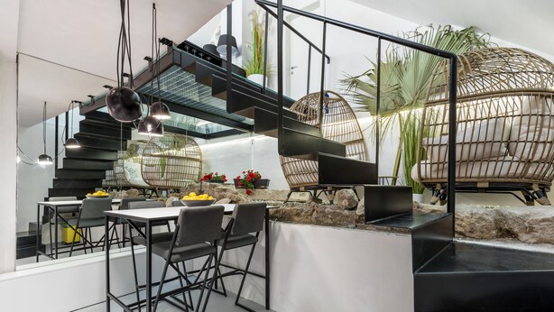 A modern interior with a staircase leading to a dining area, featuring black railings and pendant lights.