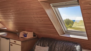 A cozy attic bedroom with a sloped ceiling, a window with a view of greenery, a wooden desk, and a cushioned bench. - Studio apartment with sea view (Grömitz)