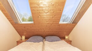 A bedroom with two beds, wooden ceiling, and skylights. - Studio apartment with sea view (Grömitz)