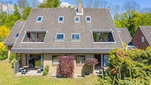 A modern two-story house with a sloped roof, large windows, and a small patio area with outdoor seating. - Studio apartment with sea view (Grömitz)