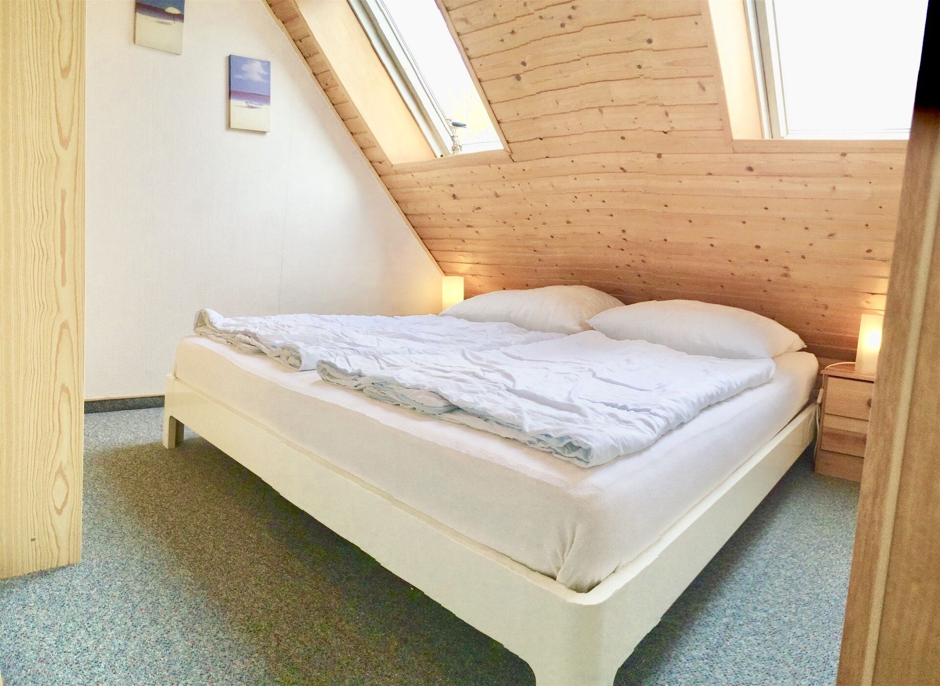 A single bed in a room with a sloped ceiling, wooden walls, and a small bedside table.