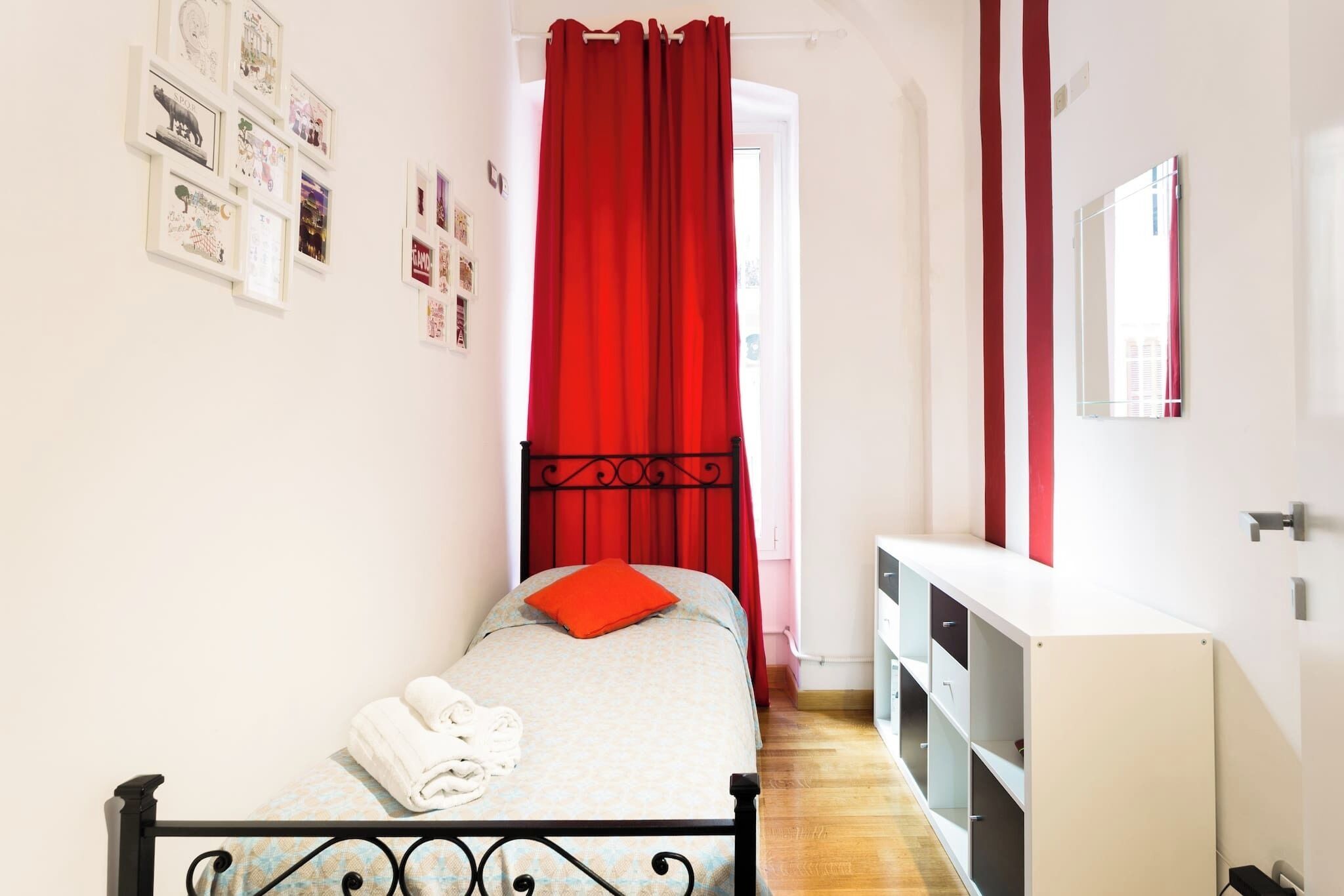 A bedroom with a bed, a white wardrobe, a red curtain, and wall art.