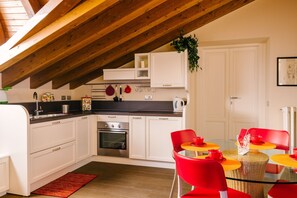 Een moderne keuken met witte kasten, een ingebouwde oven en een eethoek met rode stoelen en een glazen tafel.