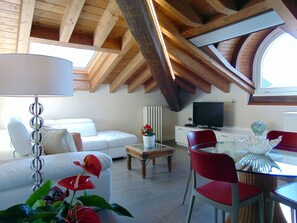 Een moderne woonkamer met een witte bank, rode fauteuils, een glazen salontafel en een televisie.
