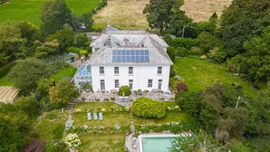 Una casa grande y blanca con techo solar, piscina y jardín bien cuidado.