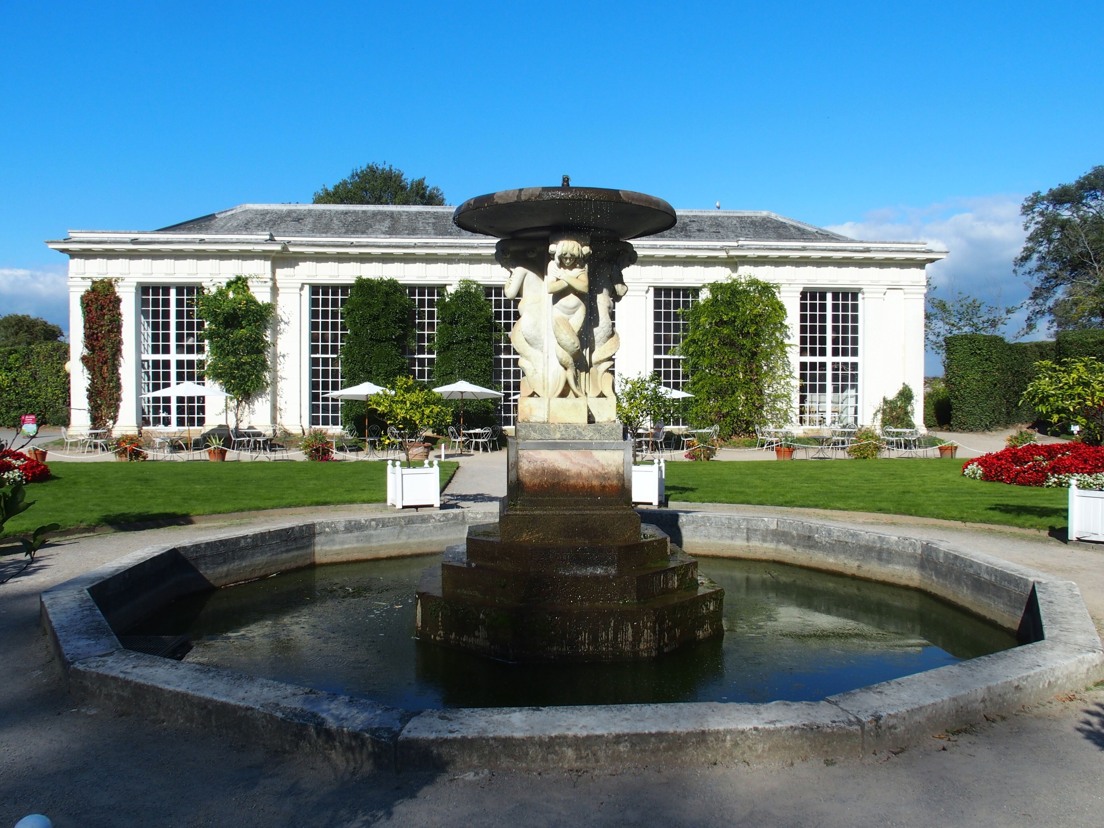 A fountain with a statue in front of a building with large windows and outdoor seating.