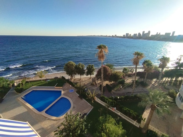 A view of a swimming pool and a beach with palm trees, overlooking a city skyline. - PRIVATE ACCESS TO BEACH IN THE SAME URBANIZATION (El Campello)