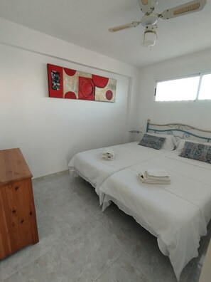 Un dormitorio con cama, ventilador de techo, ventana y mesita de noche de madera.