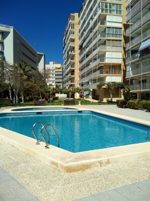 Una piscina con dos escaleras de metal, rodeada por un solárium con baldosas.