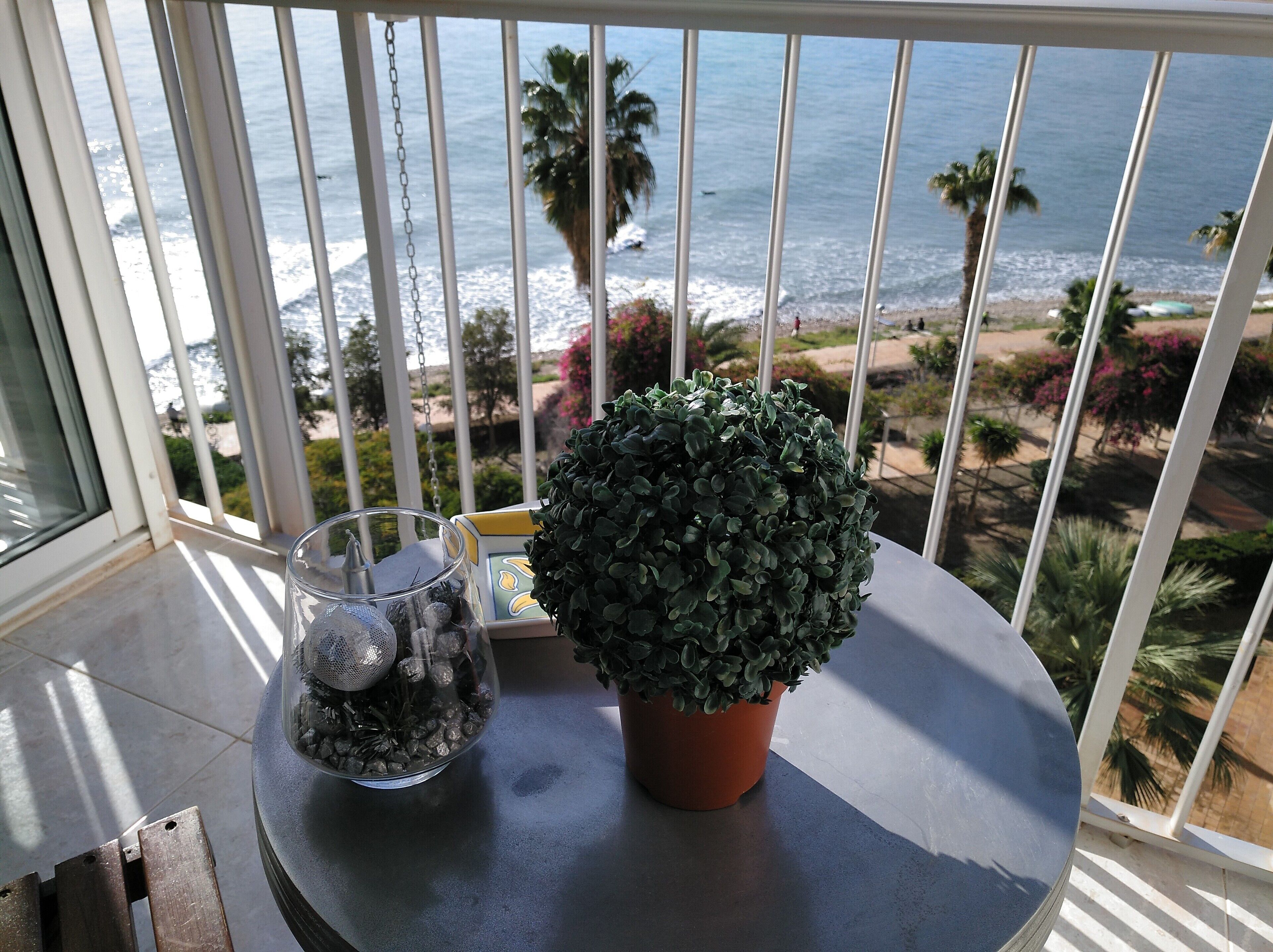 Un balcon orné d’un pot de fleurs et d’un récipient en verre contenant des objets décoratifs.
