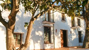 A white building with a courtyard, featuring a tree with a swing, a window with a metal grille, and a door. - A comfortable country house situated in the Natural Park, Sierra de Grazalema. (Grazalema)