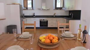 A modern kitchen with white cabinets, a black countertop, and a dining area set for four with a fruit bowl and wine bottles. - A comfortable country house situated in the Natural Park, Sierra de Grazalema. (Grazalema)
