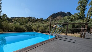 A swimming pool with a wooden deck and metal ladder, surrounded by greenery and hills. - A comfortable country house situated in the Natural Park, Sierra de Grazalema. (Grazalema)