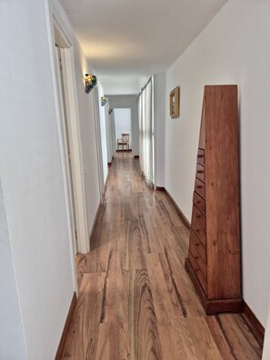 Un pasillo con suelo de madera, paredes blancas y un armario de madera.