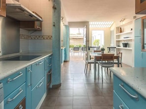 Cozinha com armários azuis, área de refeições com mesa e cadeiras, e vista para o exterior.