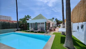 Ein Schwimmbecken mit Liegestühlen, eine überdachte Terrasse und Blick auf ein Gebäude mit Gründach.