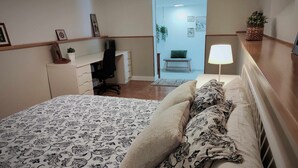 Ein Schlafzimmer mit Bett, Schreibtisch, Stuhl, Lampe und Pflanze.