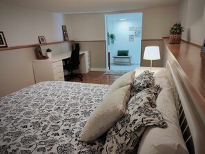 A bedroom with a bed, a desk, a chair, a lamp, and a plant.