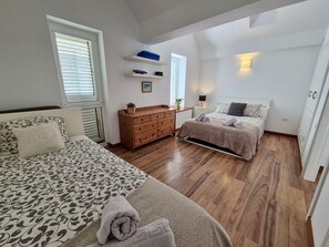 A bedroom with a bed, a dresser, a nightstand, and a window with blinds.