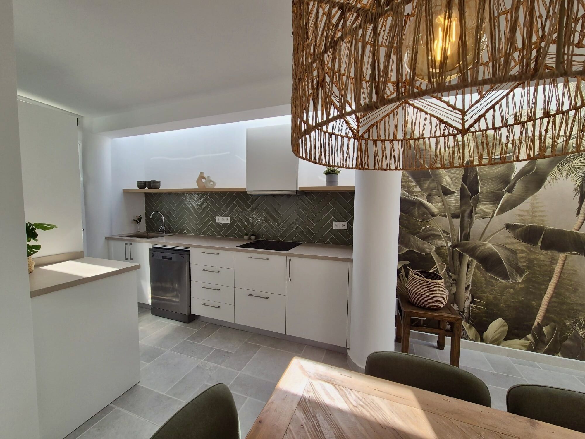 A modern kitchen with a herringbone tile backsplash, a built-in dishwasher, and a dining area with a wooden table and chairs.
