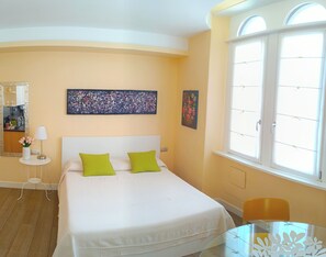 Een kamer met een bed, een klein tafeltje, een stoel, een spiegel en kunst aan de muur.